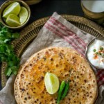 Paneer paratha served with a slice of lemon along with green chilies and a bowl of yogurt
