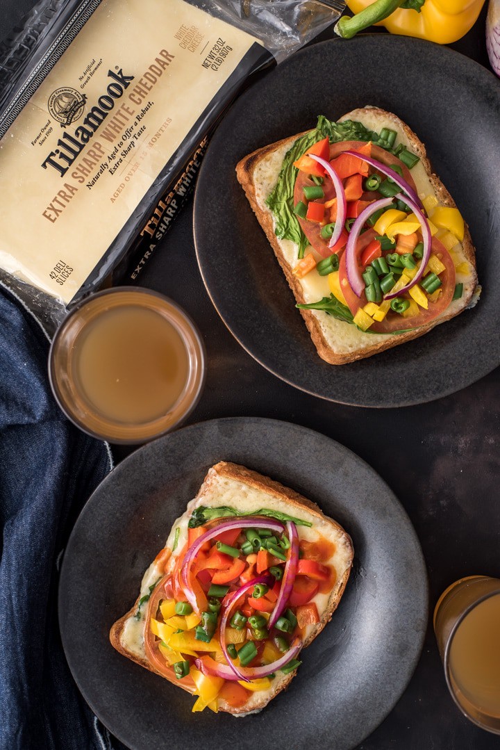 Open-faced sandwiches served in black plates. Tillamook cheese slices and two glasses of tea are kept next to them