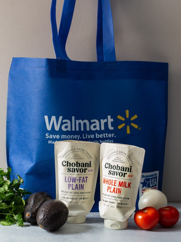 A Walmart reusable bag with cilantro on the side along with onions, tomatoes and avocados. Also. placed in front of the bag is the two flavors of Chobani Savor Topper - Whole milk and Low fat