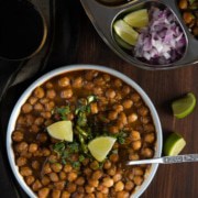 An overhead shot of chana masala sprinkled with cilantro and served with lime wedges