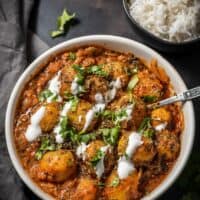 An overhead shot of Instant Pot Dum Aloo recipe served in a white bowl and garnished with fenugreek leaves, cilantro and yogurt
