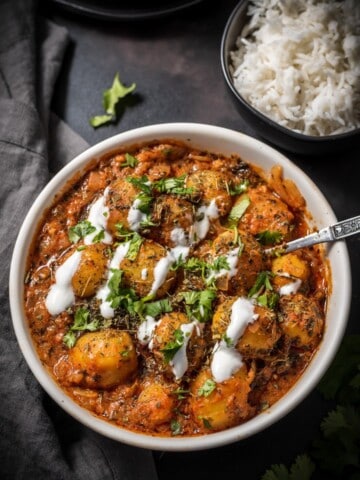 An overhead shot of Instant Pot Dum Aloo recipe served in a white bowl and garnished with fenugreek leaves, cilantro and yogurt