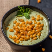 An overhead shot of mint (pudina) raita garnished with boondi and mint leaves