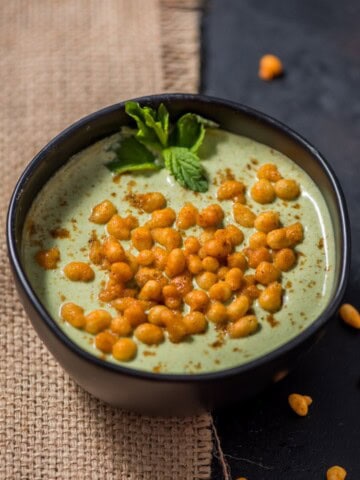 An overhead shot of mint (pudina) raita garnished with boondi and mint leaves