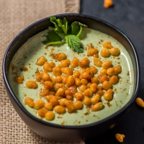 An overhead shot of mint (pudina) raita garnished with boondi and mint leaves