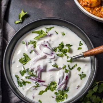 An overhead shot of onion raita served in black bowl.