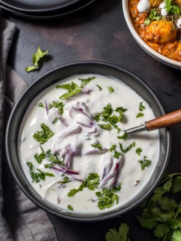 An overhead shot of onion raita served in black bowl.