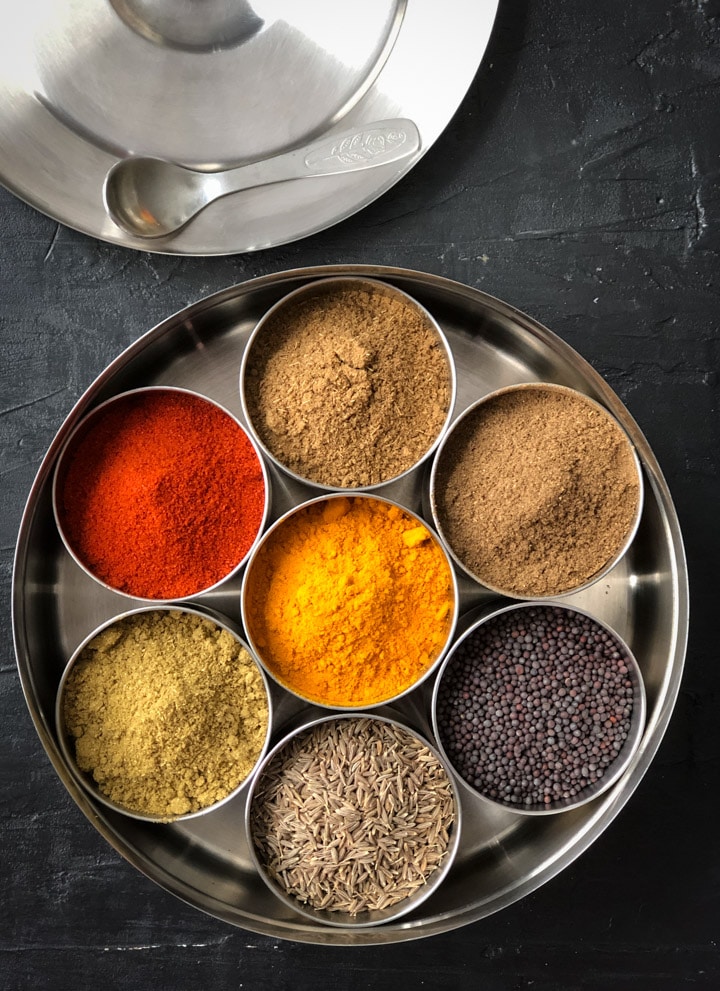An overhead shot of an Indian spice box with 7 spices in it.