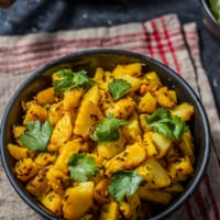 An overhead shot of Aloo jeera recipe in a black bowl. The dish is garnished with cilantro leaves.