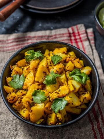 An overhead shot of Aloo jeera recipe in a black bowl. The dish is garnished with cilantro leaves.