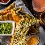 Bombay Veggie Grilled Sandwich is sprinkled with grated cheese and is served with a side of green chutney and chaat masala. A glass of raspberry lemonade is also placed on the side along with grated cheese.