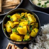Aloo sabzi served in a black bowl along with rice,roti and kadhi