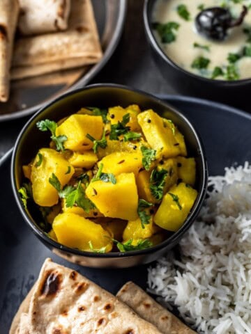 Aloo sabzi served in a black bowl along with rice,roti and kadhi