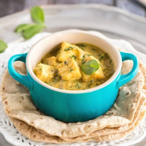 Methi Malai Paneer served in an aquamarine bowl and placed on top of a stack of rotis