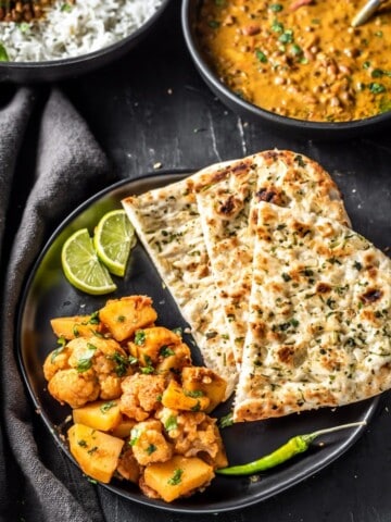 Aloo gobi served with garlic naan, green chili and lime wedges