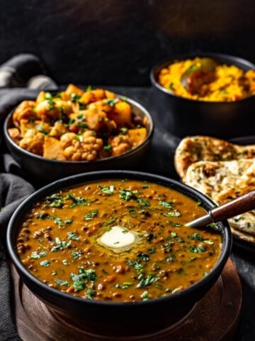 Dal Makhani served in a black bowl accompanied with aloo gobi and garlic naan