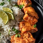 A black bowl of easy tandoori salmon with rice on the side garnished with three lime wedges and cilantro. The words quick and easy tandoori salmon typed across the top of the photo.