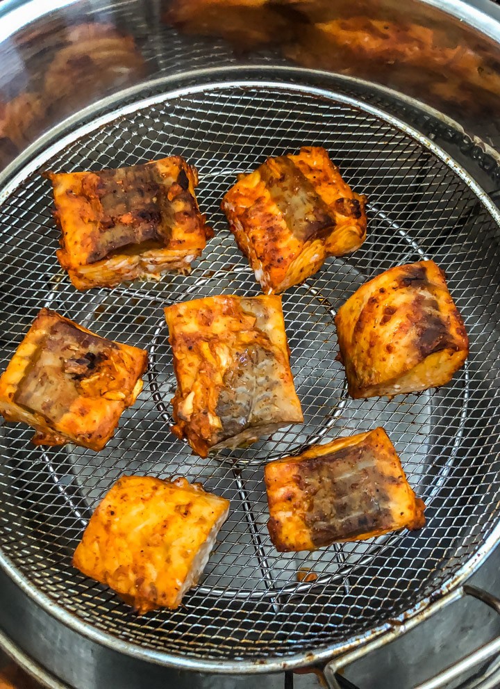 7 pieces of salmon tikka in a mesh tray cooking in the instant pot with the Mealthy CrispLid . The salmon are arranged in a circle with 6 pieces on the outside and one in the middle.