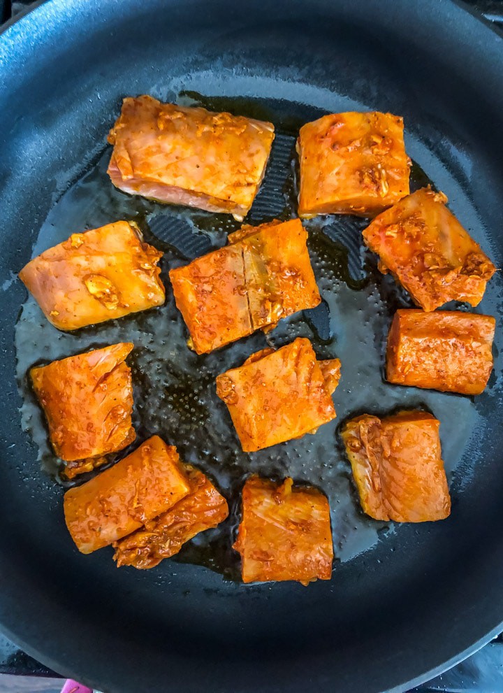 Raw salmon placed in a cooking pan on the stove top with oil cooking for the salmon tikka recipe.