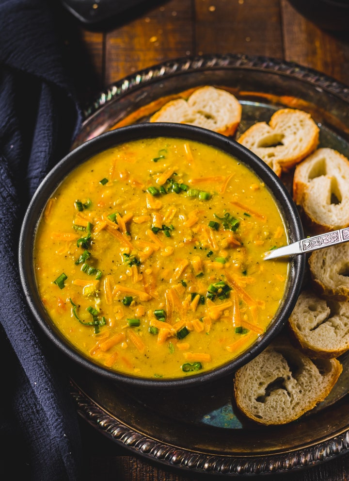 Broccoli Cheddar Soup served in a black bowl accompanied by baguettes