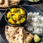 A black plate with rice, lemon wedges and potato side dish. A caption over the image reads Indian cooking basics learn more