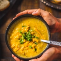 Two hands cupping a black bowl filled with cheesy Broccoli Cheddar Soup