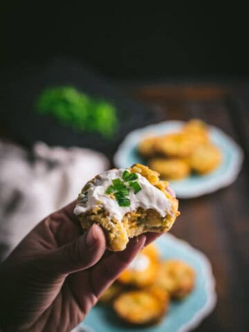 A hand holding a mashed potato muffin topped with sour cream
