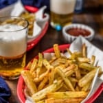 Two red baskets of air fried french fries with a denim napkin, ketchup, and a small pint glass of beer with the words Crispy Air Fryer French Fries typed in white on the top.