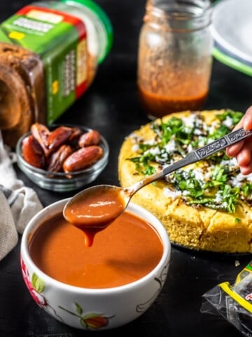 Hand holding a spoon of tamarin chutney which is accompanied by Khaman