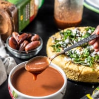 Hand holding a spoon of tamarin chutney which is accompanied by Khaman