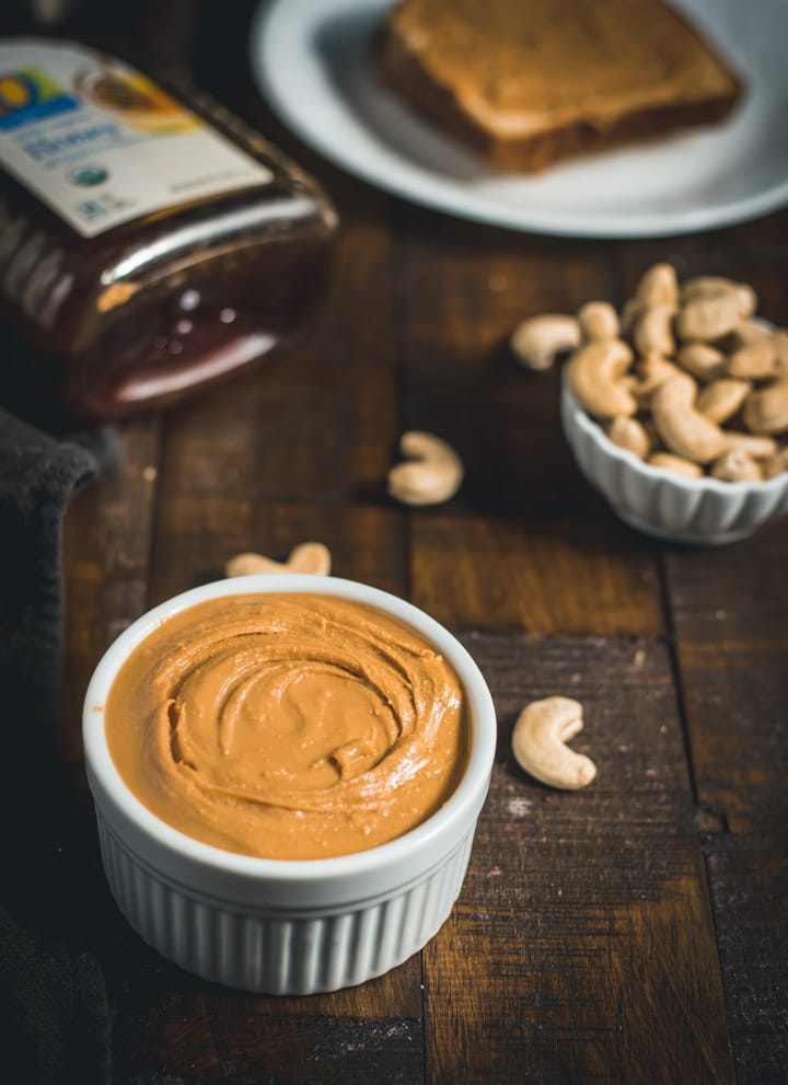 Cashew butter served in a ramekin with cashew pieces and a bottle of honey on the side