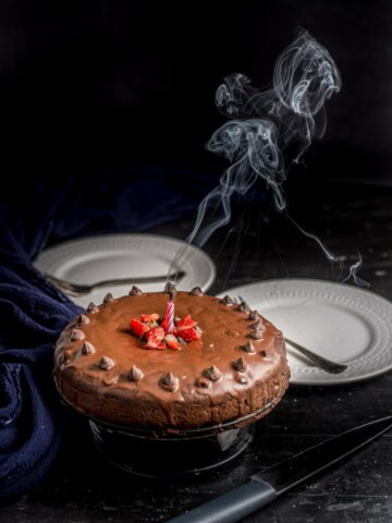 A cakey brownie on a cake stand with a candle blown out and smoke in the air.