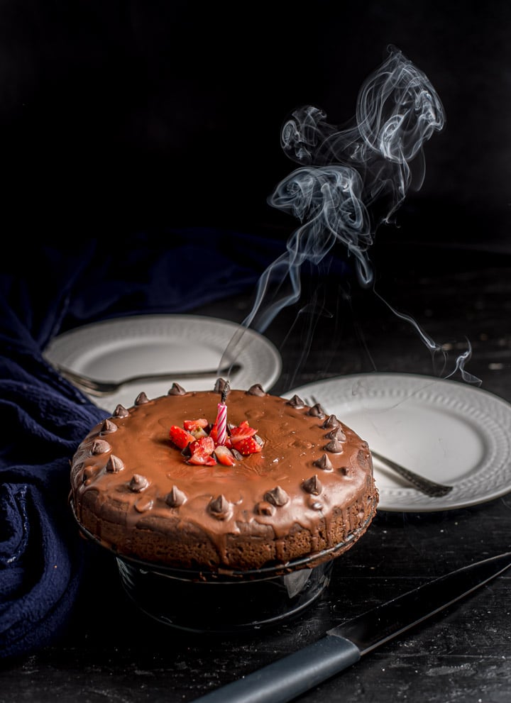 A cakey brownie on a cake stand with a candle blown out and smoke in the air.