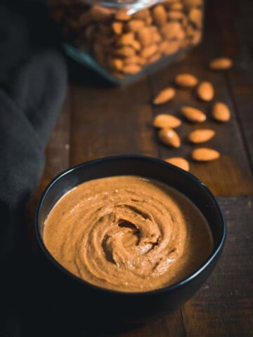 Almond Butter served in a black bowl with almonds placed on the side