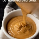 A white bowl with creamy homemade peanut butter being poured into it on white dish towel and the words Easy Homemade Peanut Butter at the top.