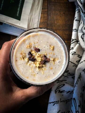 An overhead shot of a hand holding a glass of apple banana smoothie