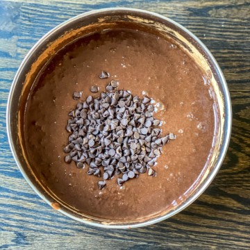 A mixing bowl with condensed milk, cocoa, and chocolate chips stirred together.