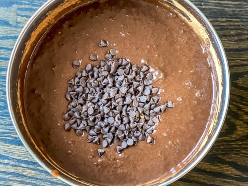 A mixing bowl with condensed milk, cocoa, and chocolate chips stirred together.