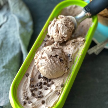 A green tub of double chocolate ice cream with an ice cream scoop and two scoops of ice cream.
