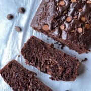 A loaf of chocolate zucchini bread sliced with two slices in the front on a sheet of parchment paper with the words chocolate zucchini bread at the top.