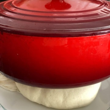 A red cast iron skillet sits on top of a cheesecloth with homemade paneer inside to drain and shape the cheese.