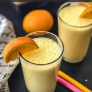 Two glasses of orange smoothie with wedges of orange on the rim, two colorful straws in the middle of the smoothie cups, and an orange in the back and the words Orange Creamsicle Smoothie at the top.