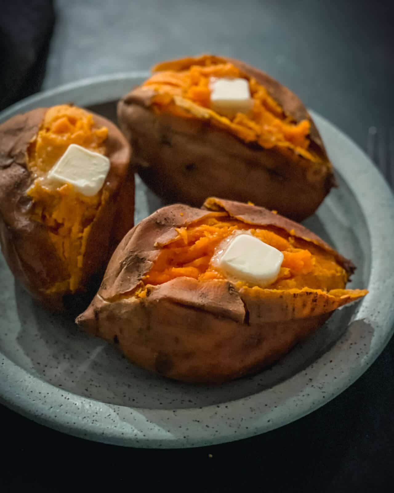 Three baked sweet potatoes cut down the middle with a pad of butter on top on a blue plate.