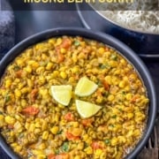 The words Instant Pot in white and Moong Bean Curry in yellow at the top with a large black bowl of Moong bean curry on a table with a fork to the right.