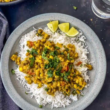 A grey plate with mung bean curry on top of rice and 3 wedges of lime on the plate.