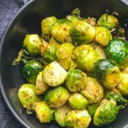 The words Steamed and Sautéed Brussel Sprouts at the top with a black bowl of bright green steamed and sautéed Brussel sprouts on a grey counter.