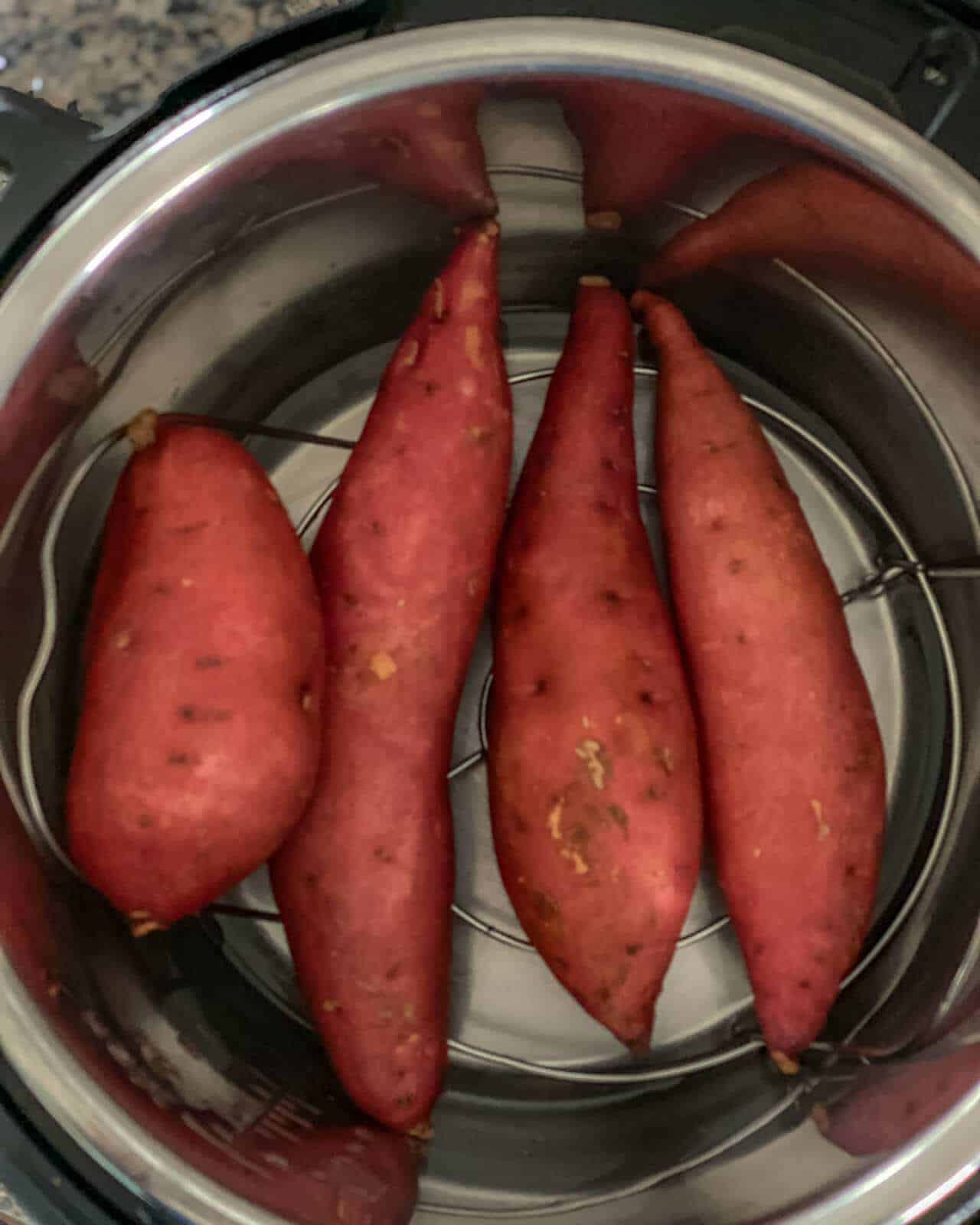 Four sweet potatoes on a trivet inside an instant pot pressure cooker.