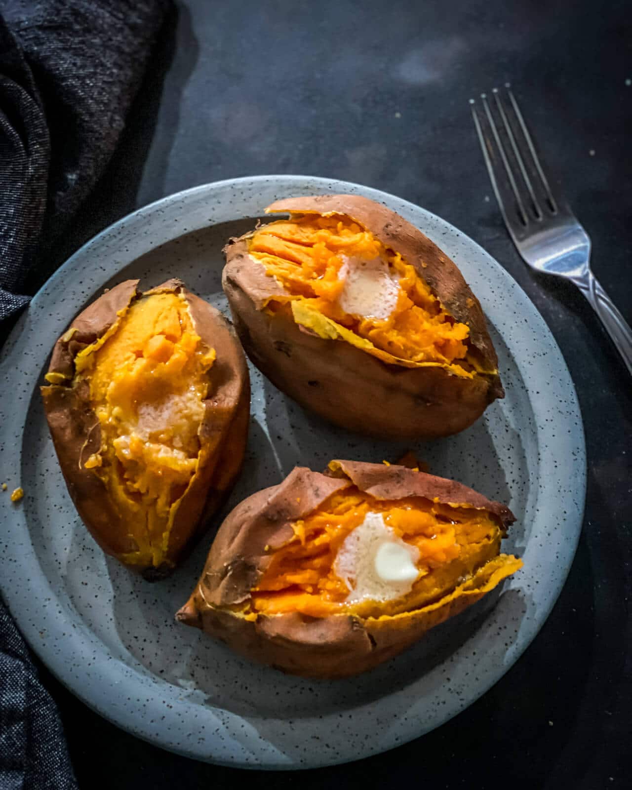 3 sweet potatoes that are split open placed in a grey plate topped with butter