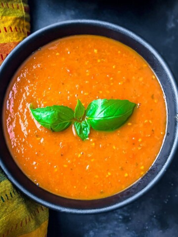 A black bowl on a grey counter with a colorful napkin to the left and marinara sauce with basil leaves in the bowl.