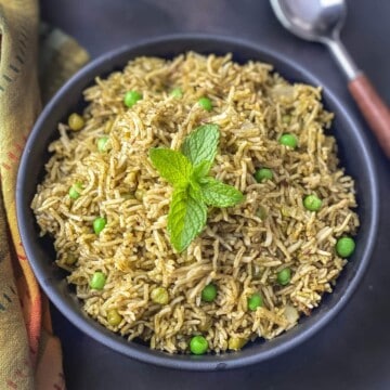 A dark grey bowl with palak rice and peas topped with fresh mint leaves.